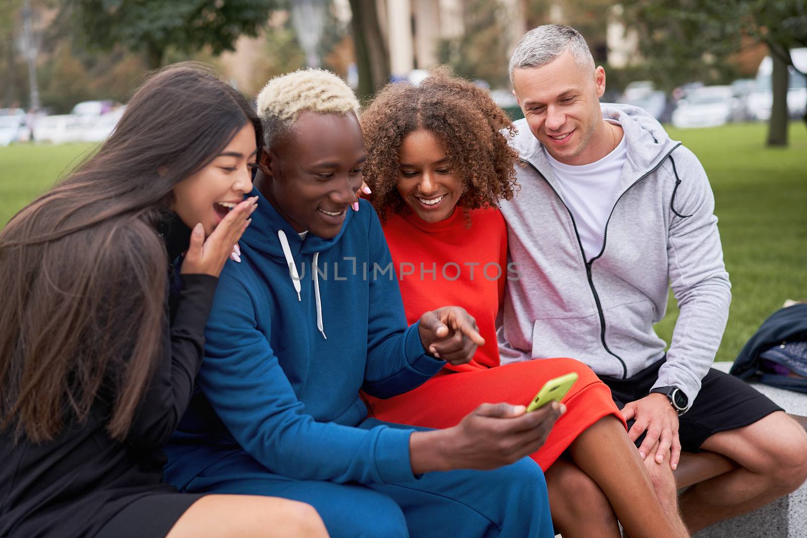 Multi ethnic friends outdoor looking smartphone screen. Diverse group people Afro american asian caucasian spending time together Multiracial male female student sitting bench park outdoors