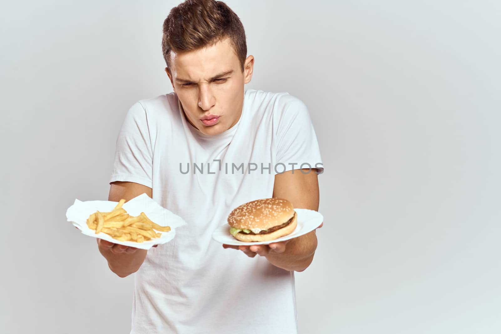 a man with fries and a hamburger on a light background in white t-shirt close-up cropped view Copy Space Model. High quality photo