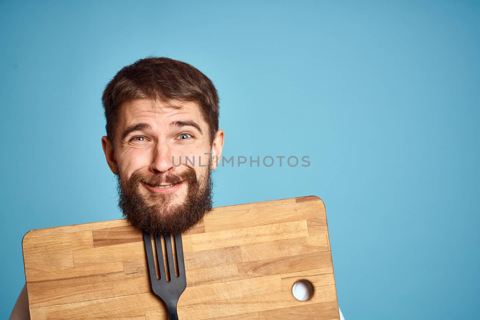 cute man with kitchen board near face on blue background emotions smile model. High quality photo