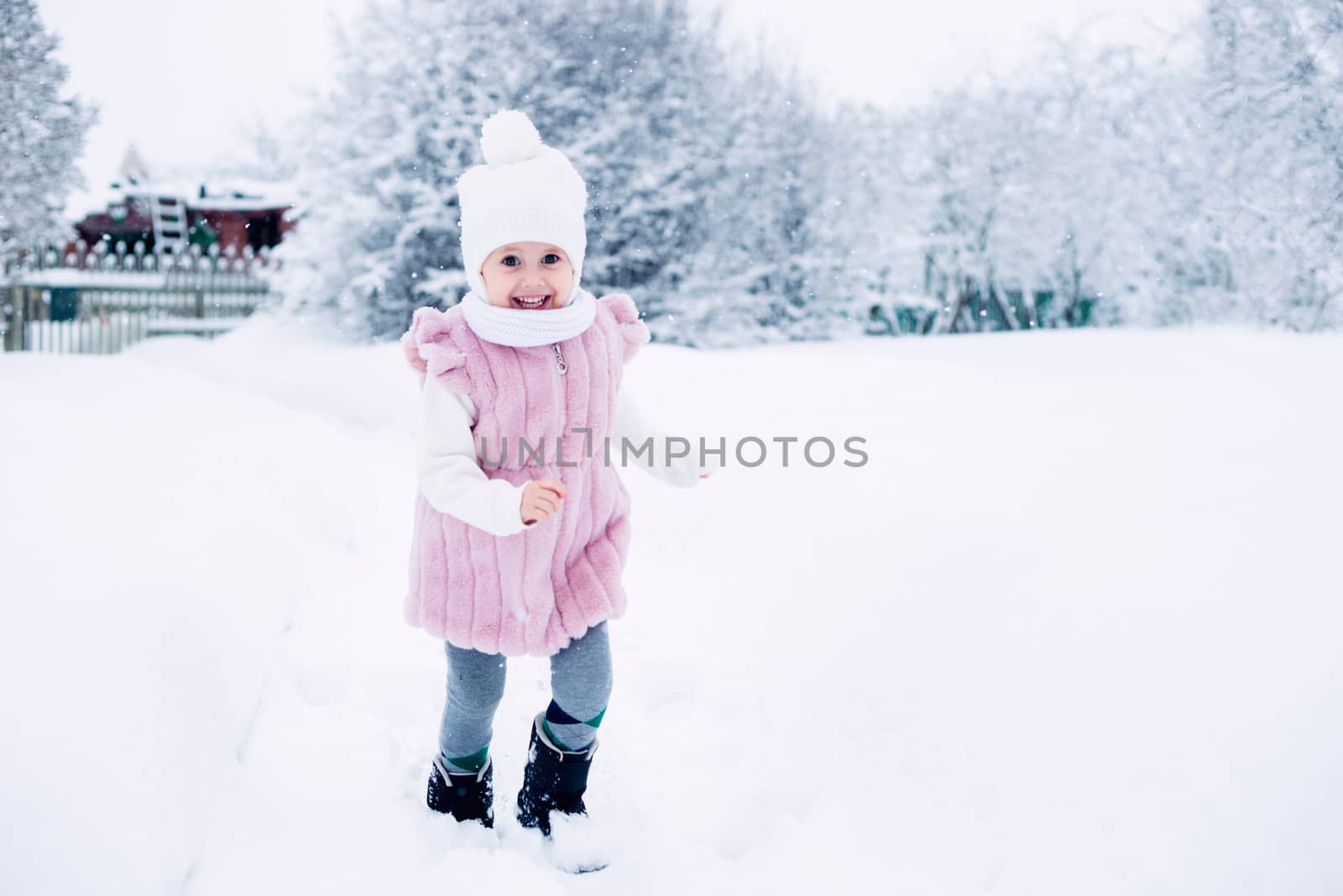 .A little girl in a pink fur coat stands in the middle of a snow-covered park by galinasharapova