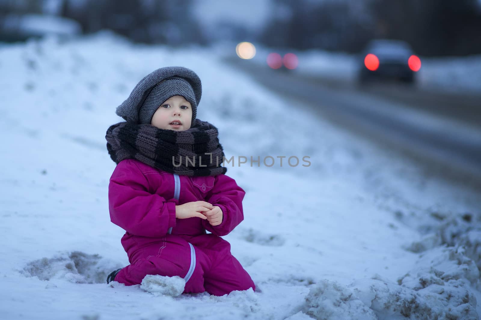 A little girl sits in the snow by the road and watches passing cars by galinasharapova