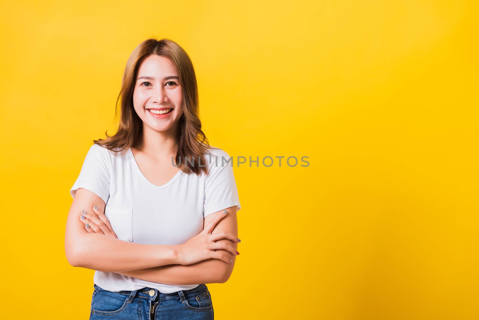 Asian Thai happy portrait beautiful cute young woman standing wear t-shirt her smile confidence with crossed arms looking to side up isolated, studio shot on yellow background and copy space