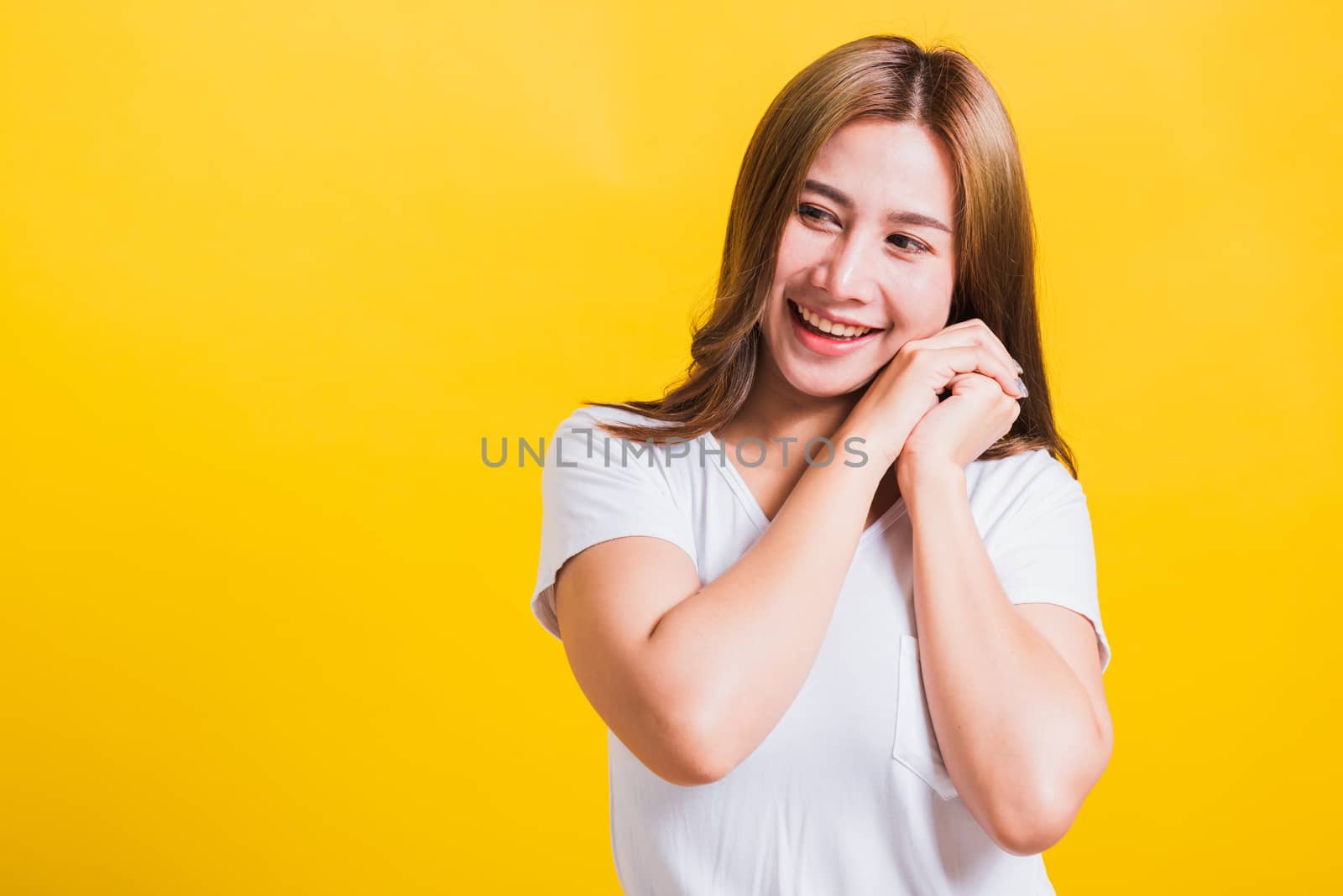 Portrait Asian Thai beautiful happy young woman smiling, screaming excited keeps two hands together near the face and looking to side, studio shot isolated on yellow background, with copy space