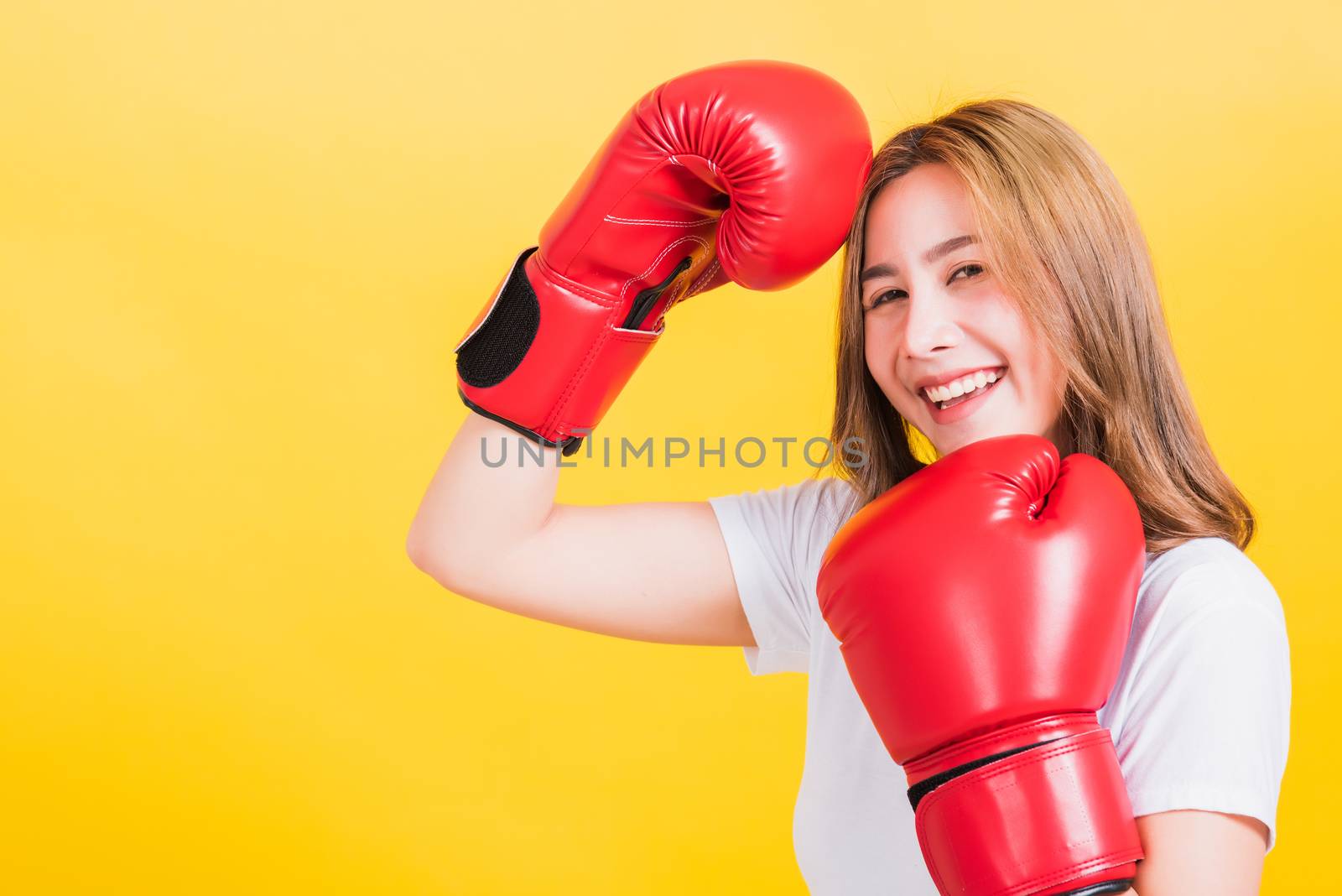 Portrait Asian Thai beautiful young woman standing smile wearing red boxing gloves she poses like a boxer, studio shot isolated on yellow background, There was copy space for text