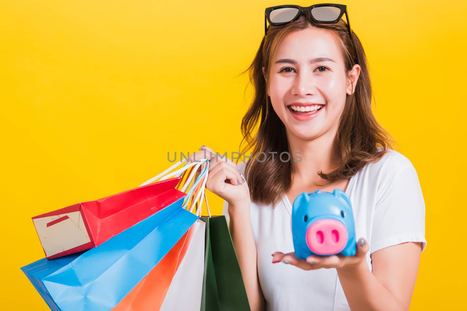 Portrait Asian Thai beautiful young woman happy hold colorful shopping bags and Piggybank Saving money, studio shot isolated on yellow background, with copy space