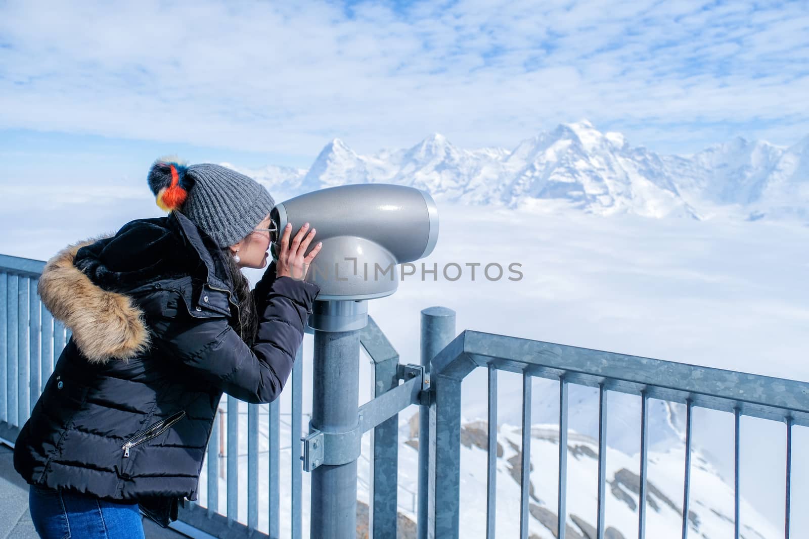 Young Woman Tourist at the Schilthorn using coin operated binocular to enjoy the magnificent panoramic view of the Swiss Skyline.