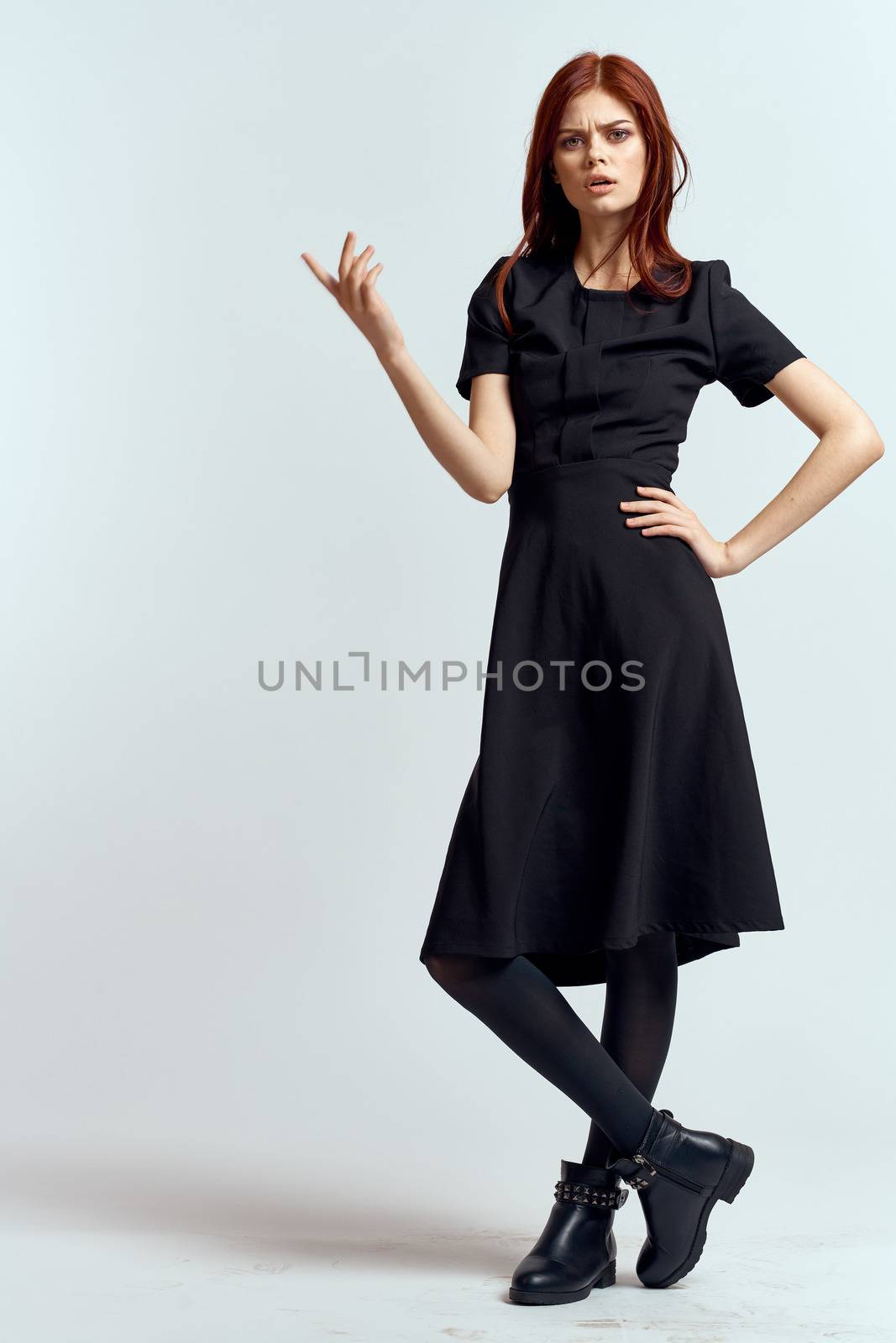 A woman in a black dress on a light background and pantyhose shoes red hair and pose in full growth. High quality photo