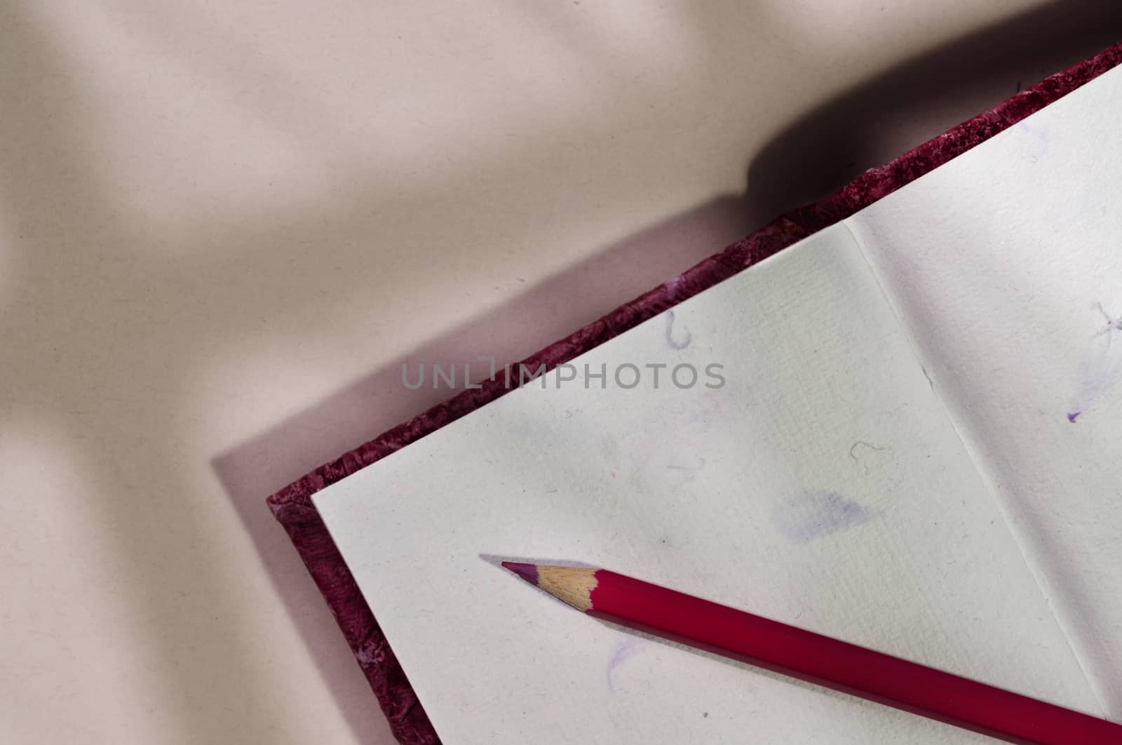 Opened notebook with red colored pencil , beautiful shadows on table , textured notebook pages