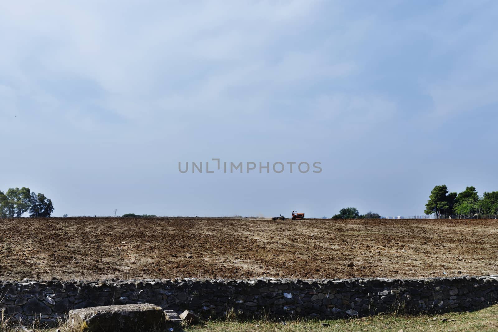 Ploughing the fields with old tractor against bright sky ,in the foreground a wall