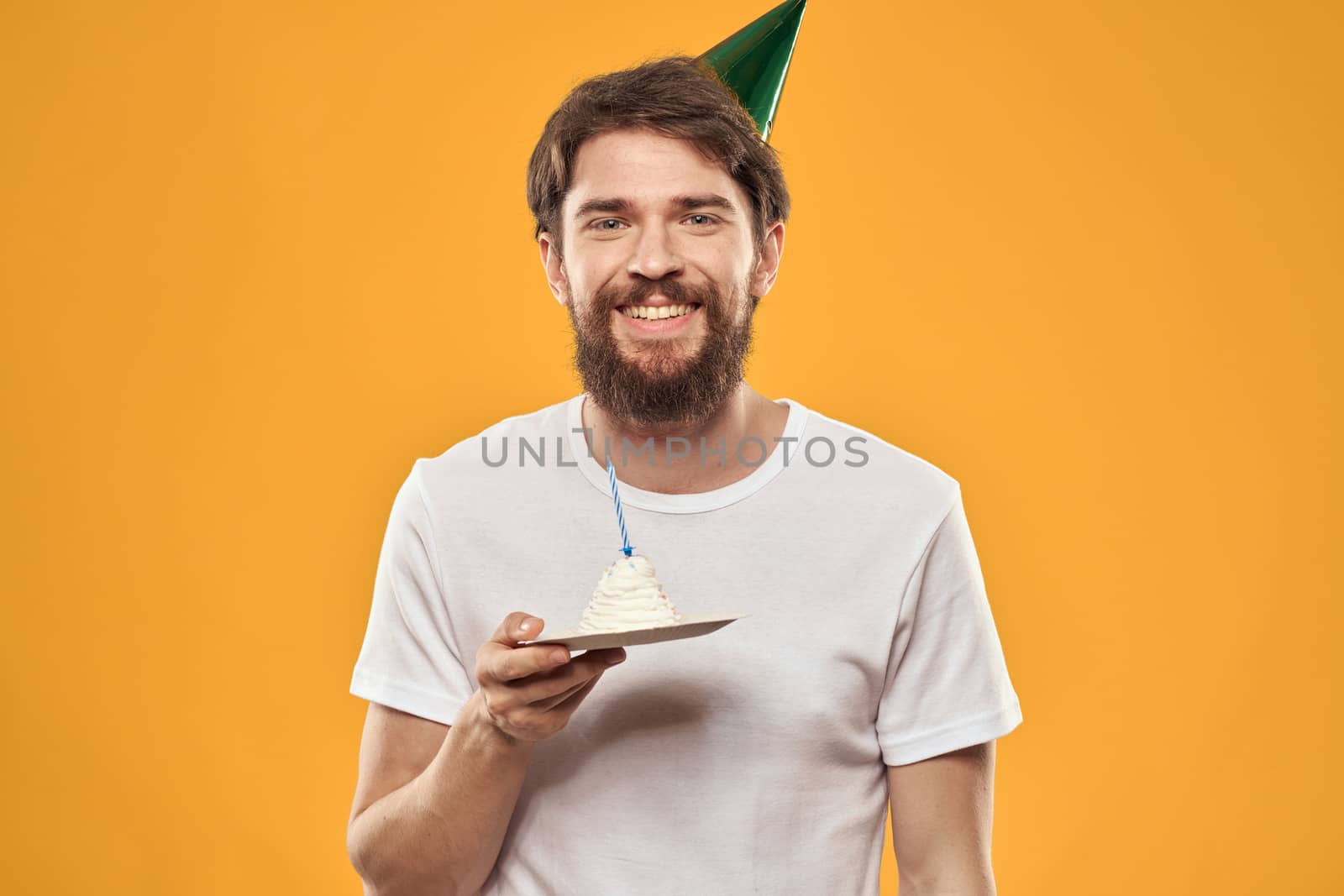 Handsome man with a beard and in a cap celebrating a birthday party yellow background. High quality photo