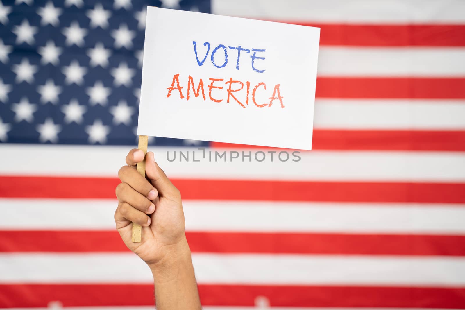 Hand Holding Vote America Sign boards with US Flag as Background - Concept of US election and Importance of Voting