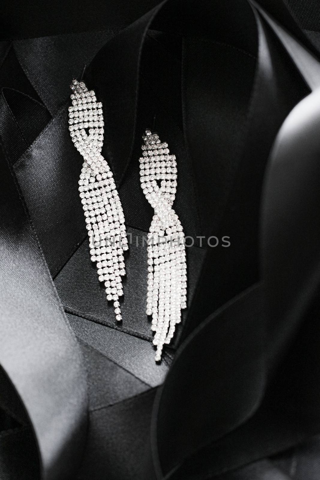 Luxury diamond earrings on black silk ribbon as background, jewelry and fashion brands