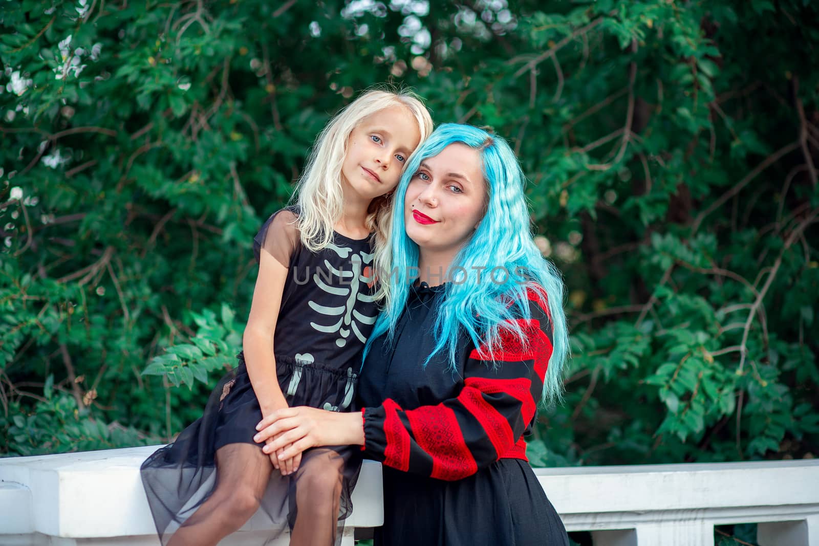 Young woman with blue hair hugging her daughter in a dress with a patterned skeleton by borisenkoket