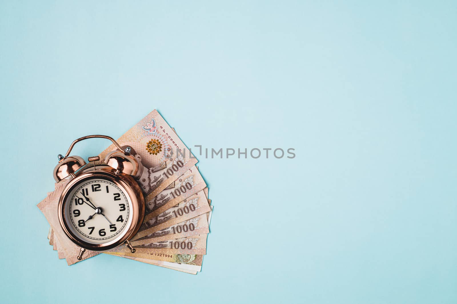 Bell alarm clock  with Thai currency, 1000 Baht, money banknote of Thailand on blue background for business, finance and time management concept