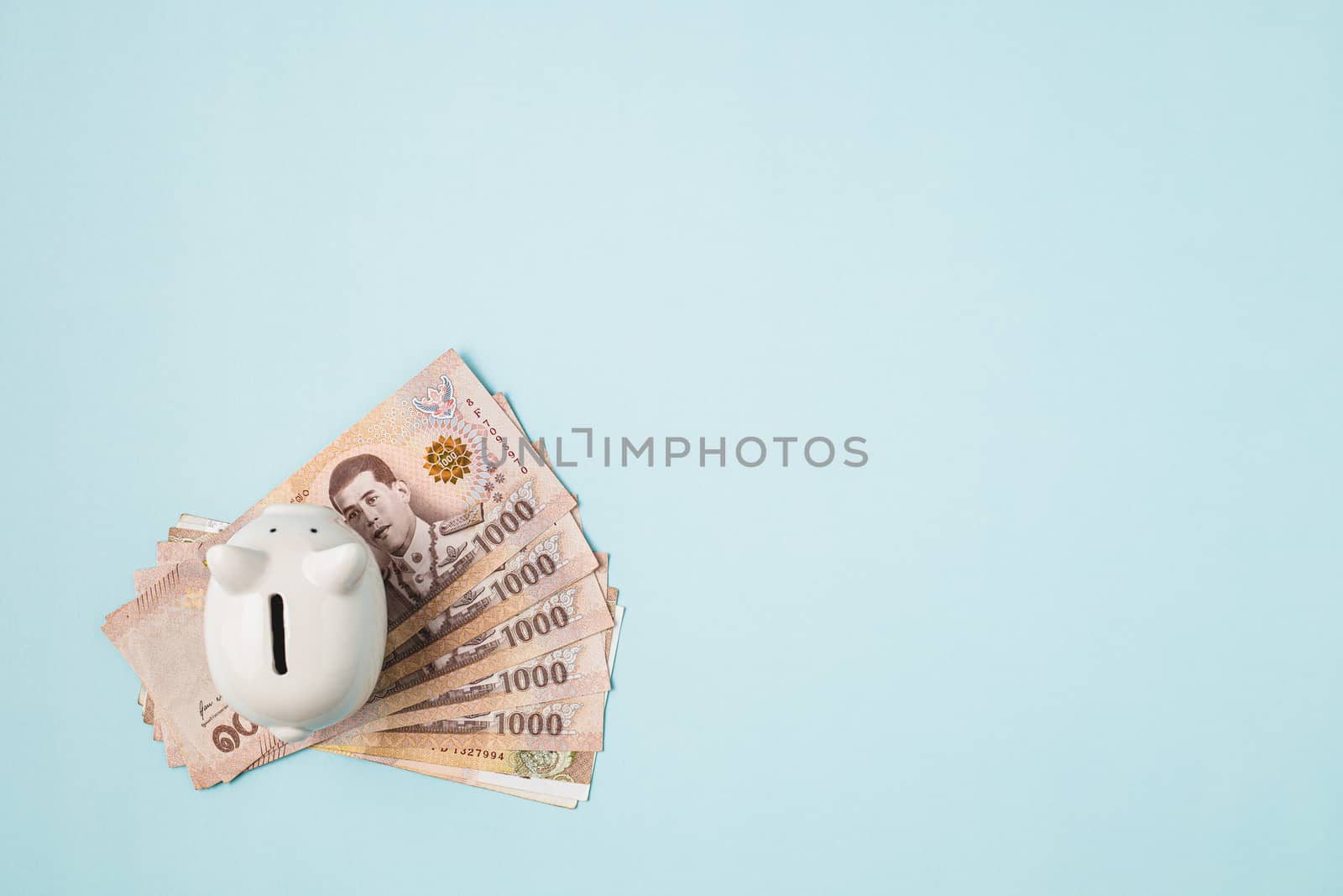 Saving piggy bank with Thai currency, 1000 Baht, money banknote of Thailand on blue background for business and finance concept