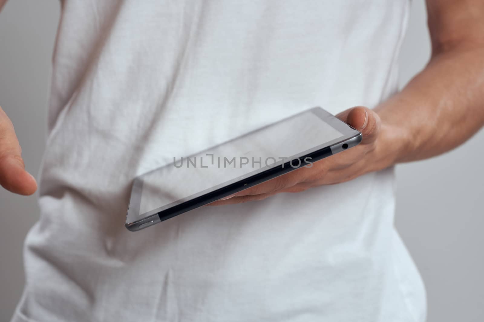 Tablet with a touch screen on a light background male hands white t-shirt cropped view. High quality photo