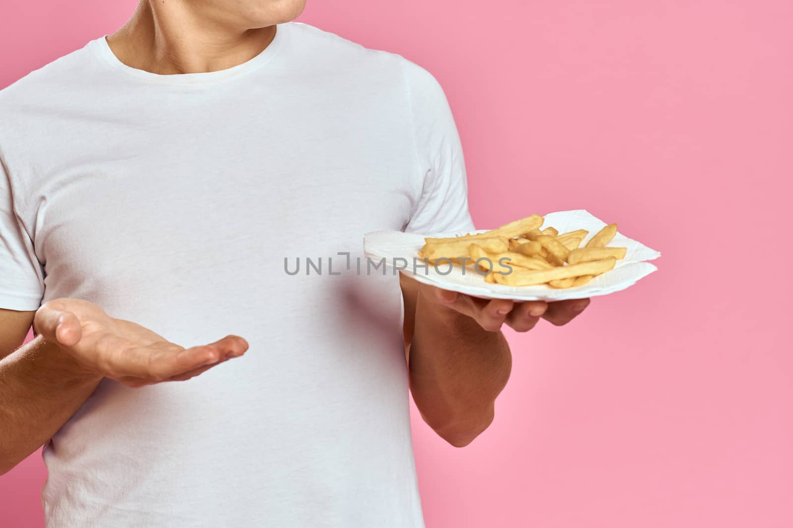 Man with French fries in a paper box on a pink background calories fast food portrait pink background. High quality photo