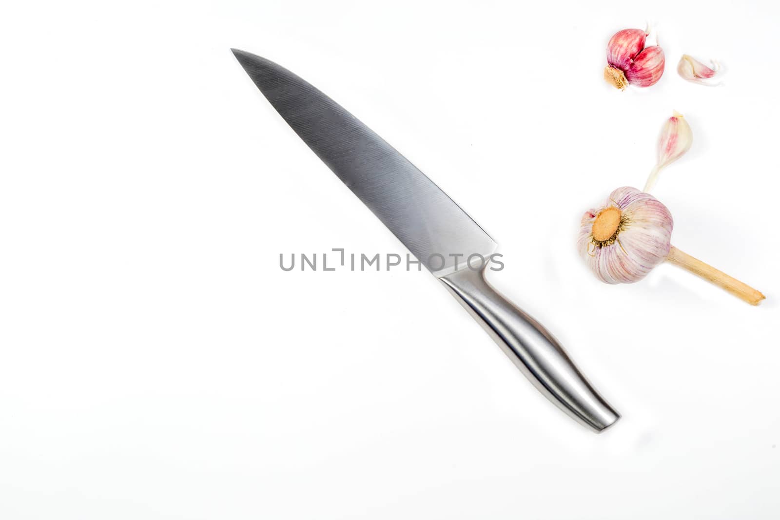Closeup image of chief knife and garlic on white table
