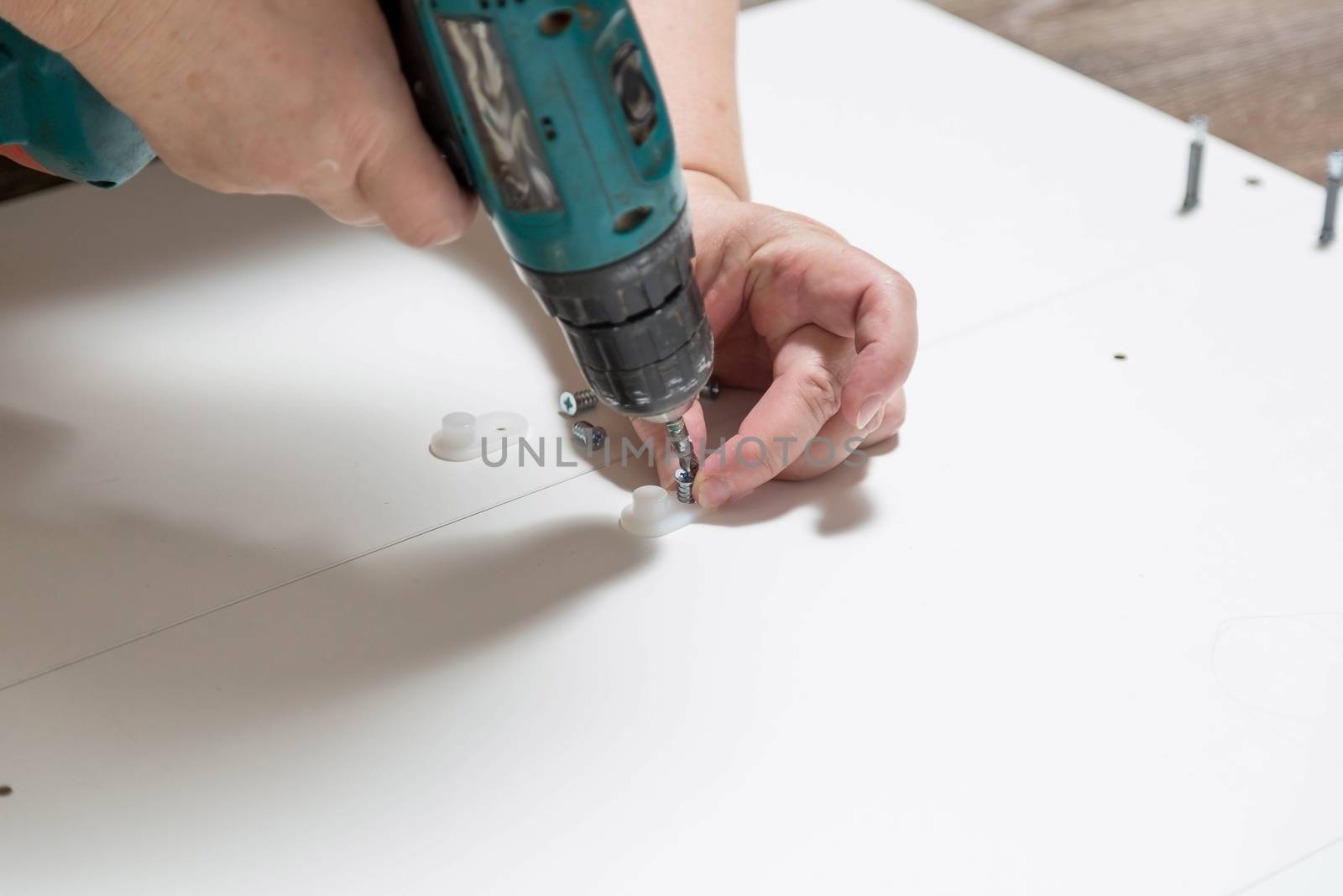 Electric screwdriver with cruciform bat wraps into furniture cabinet, screws lie nearby during assembly of purchased furniture.