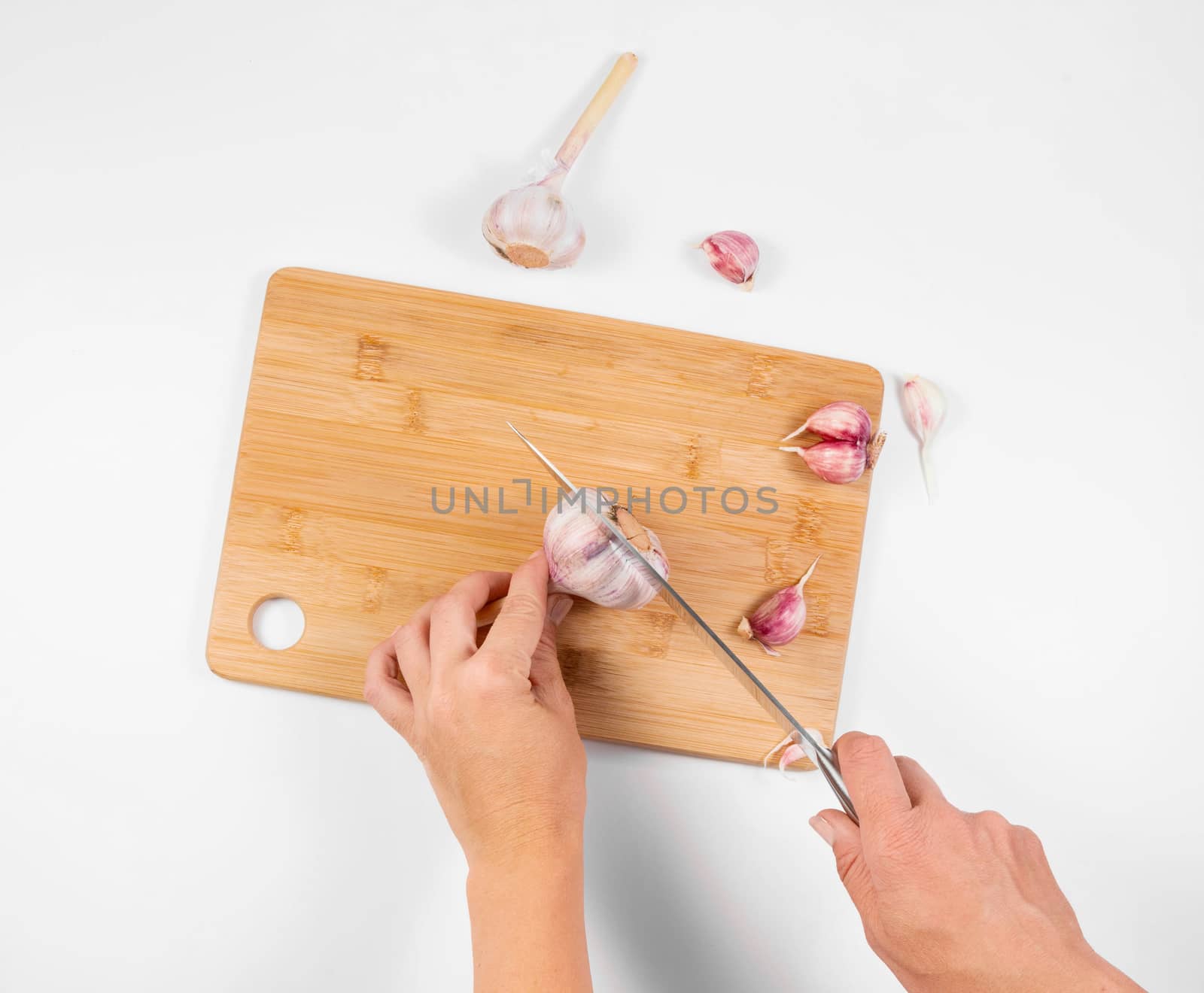 Closeup image of a woman cutting and chopping garlic by knife on wooden board