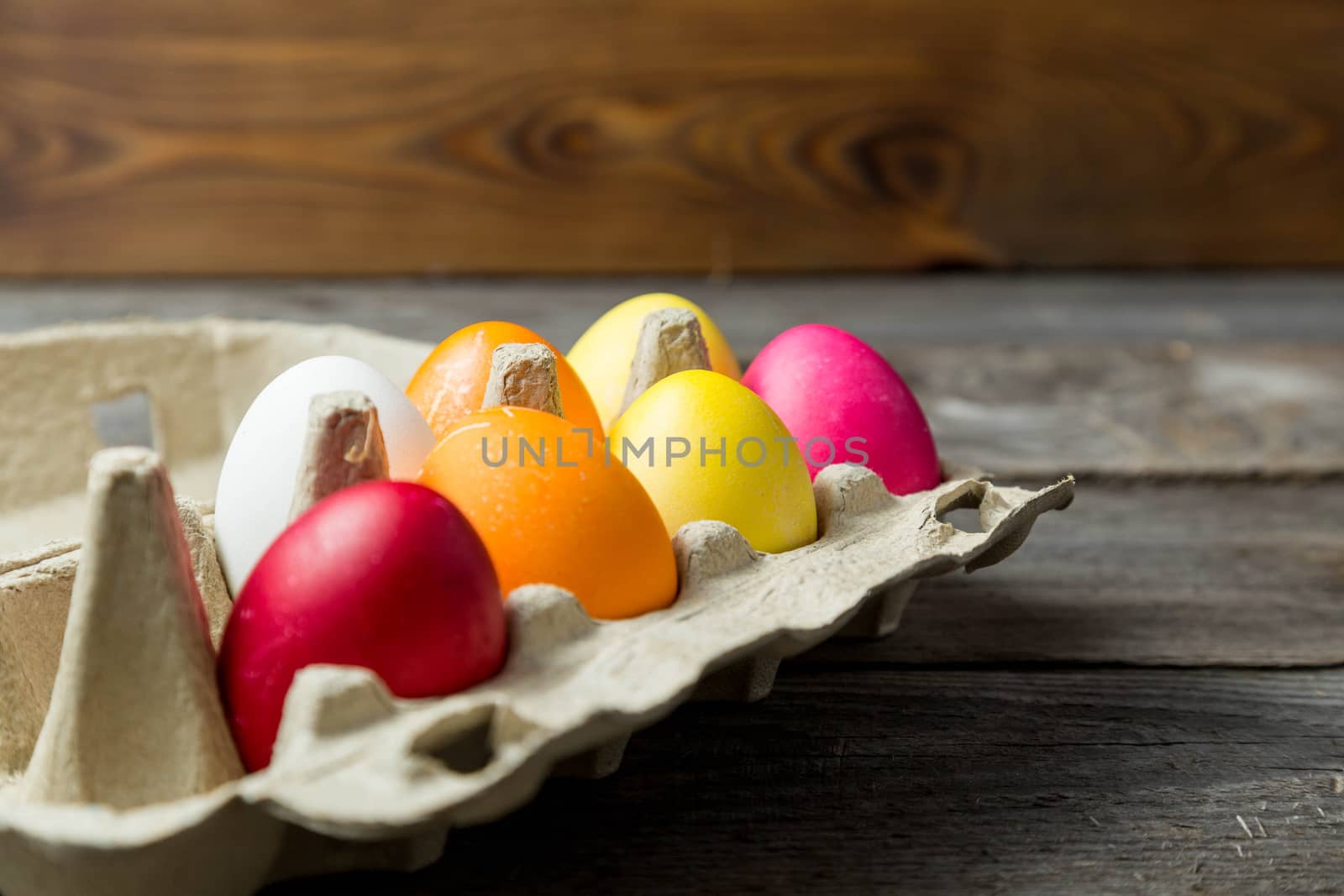 Dyed easter eggs in cardboard box on wooden background. by galinasharapova