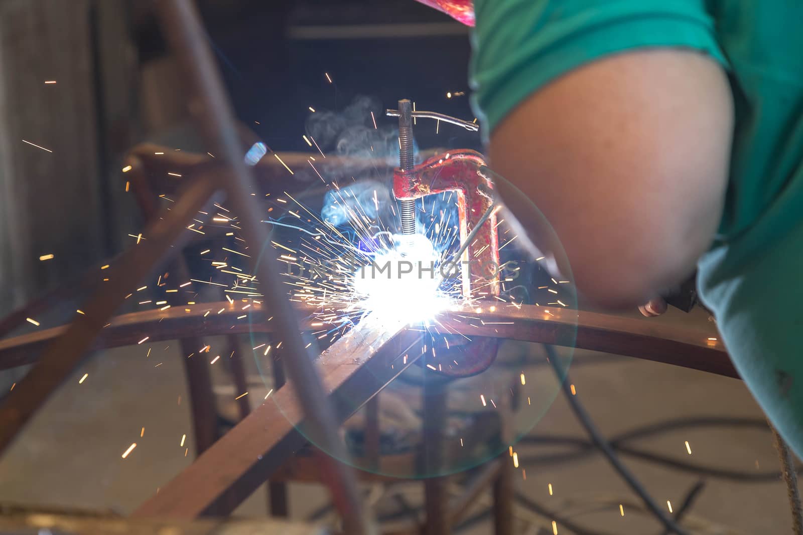 Close-up of hands A man holding a welding machine and doing spot welding under the canopy of his garage. Sparks fly away. No protective gloves on hands.