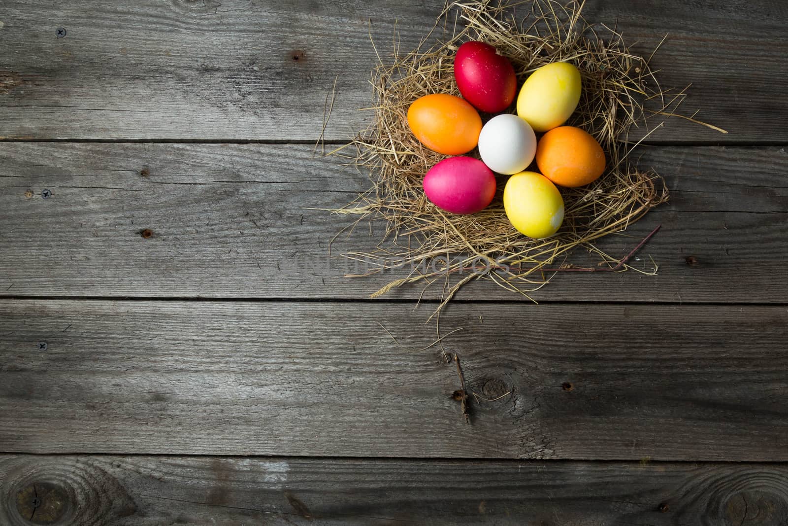 .Painted easter eggs in a makeshift straw nest on a wooden background by galinasharapova