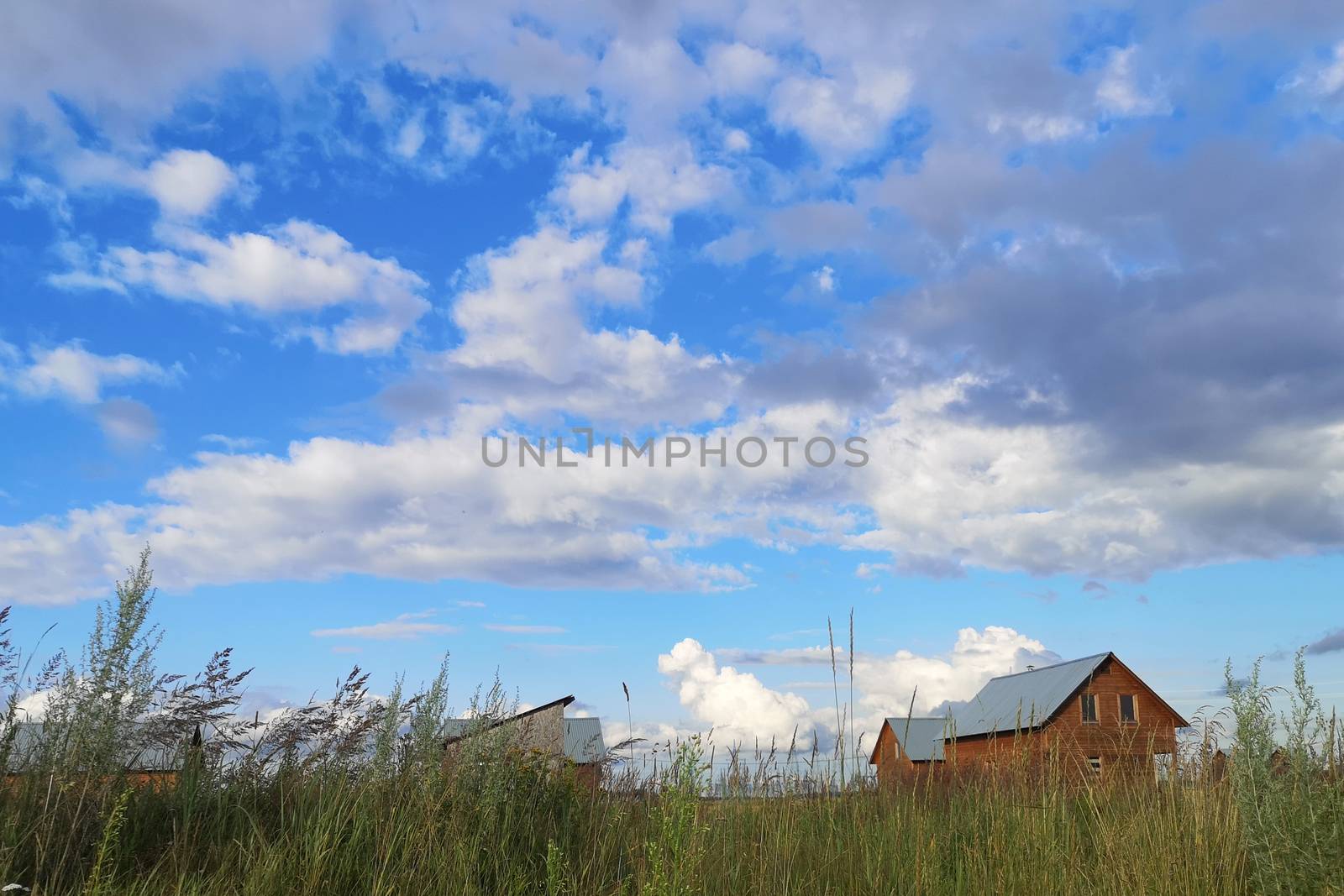 Large white clouds in the blue sky above a village in Russia.