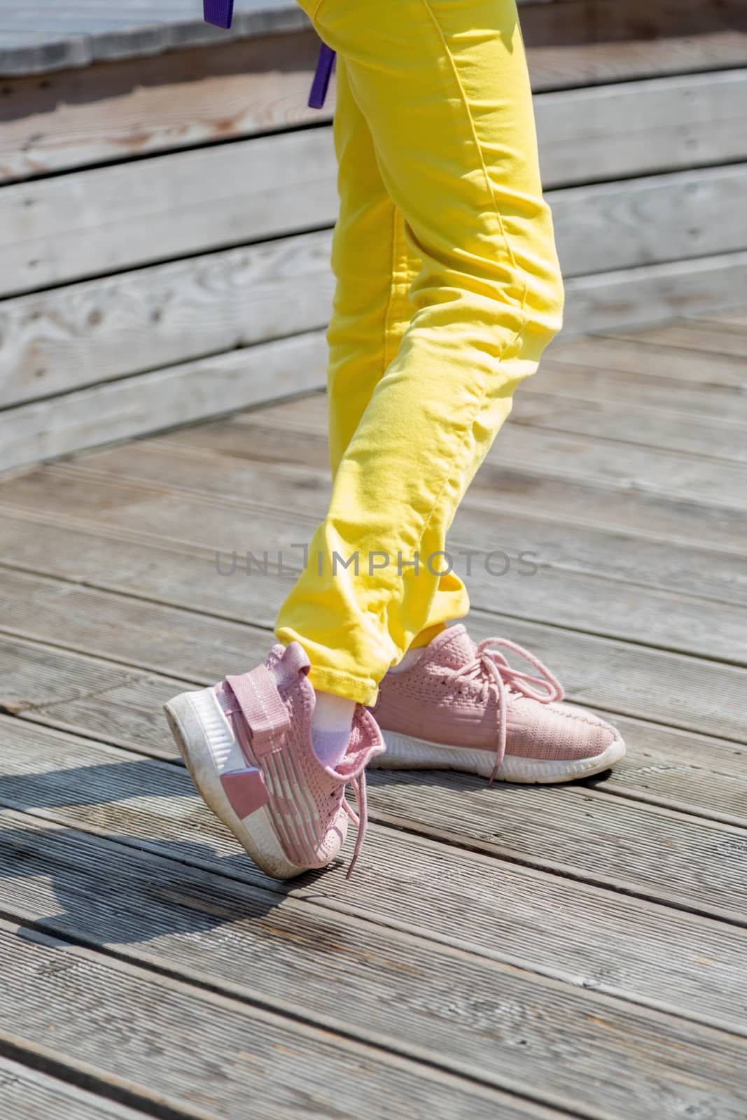 legs of a girl in yellow jeans and pink sneakers in a summer park