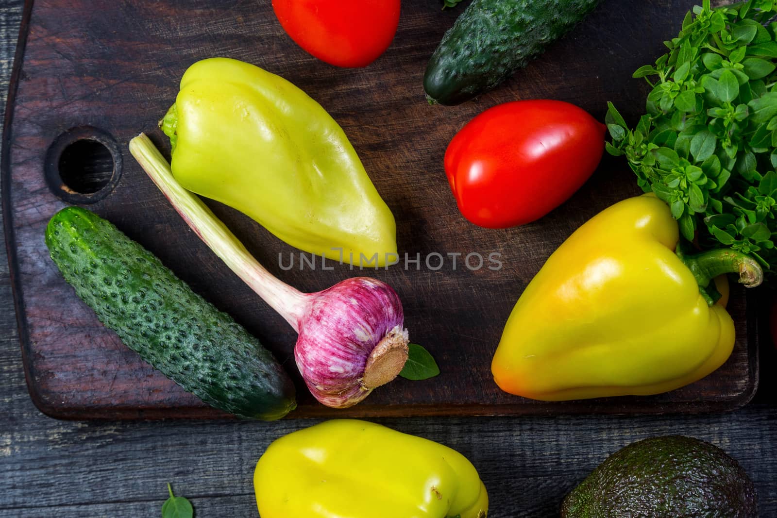 High Angle Still Life View of Wooden Cutting Board Surrounded by Fresh Herbs and Assortment of Raw Vegetables on Rustic Wood Table