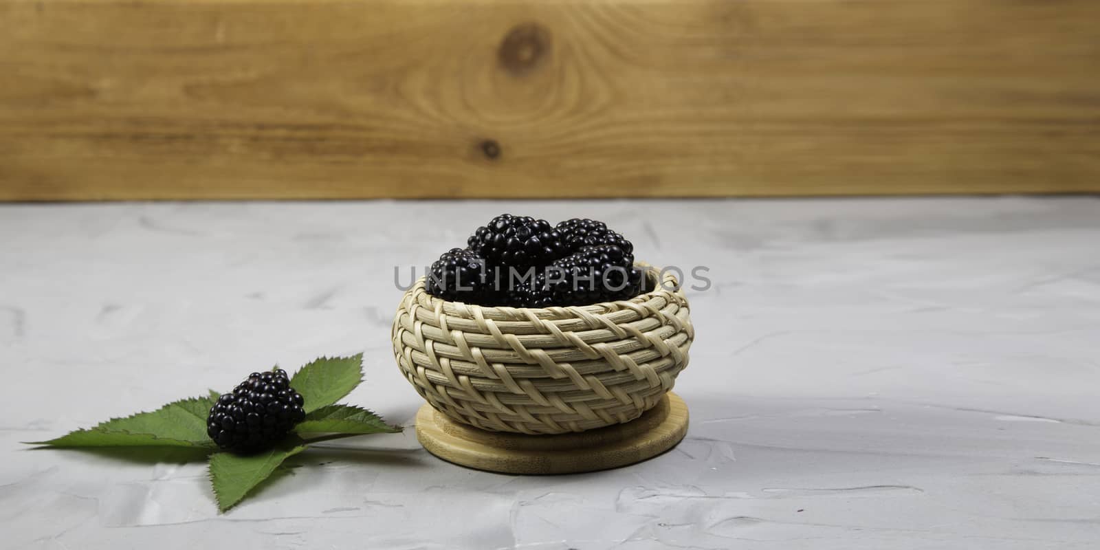 Ripe sweet blackberry in wooden wicker bowl on gray concrete background.