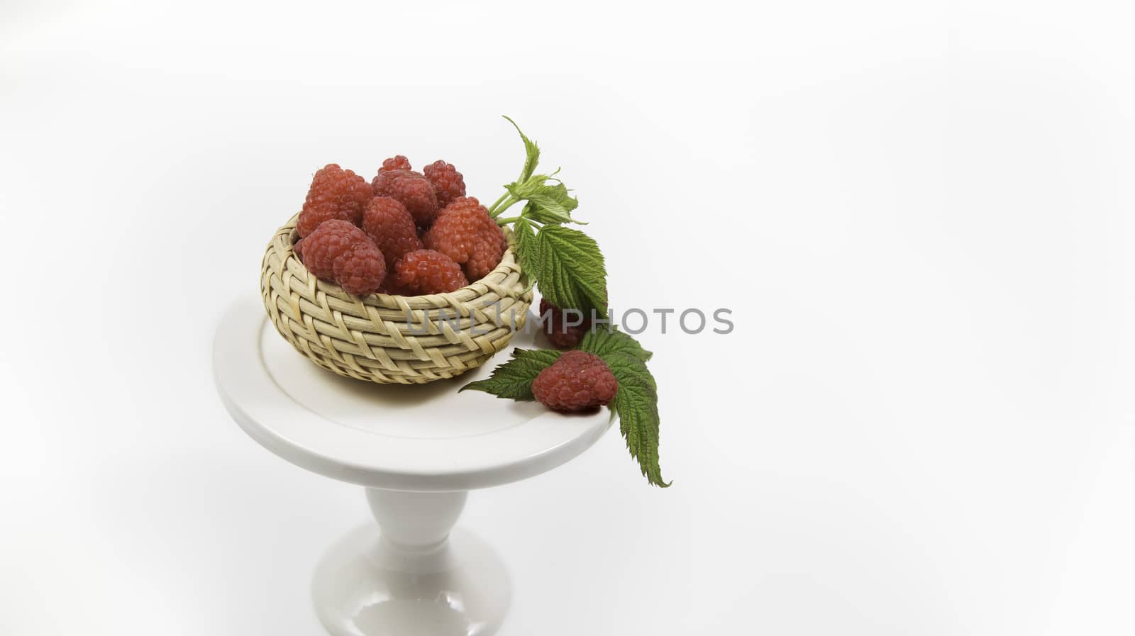 Ripe tasty bright Fresh raspberry in a wicker basket on cake stand on a white background. High quality photo