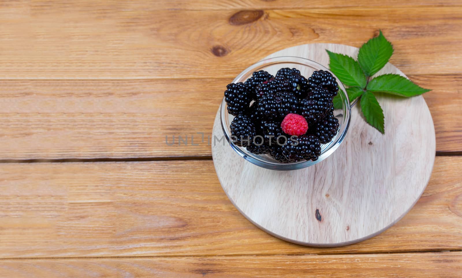 ripe blackberry with leaves on a wooden cutting board in a white ceramic bowl on dark blue wooden background. top view, place for text,