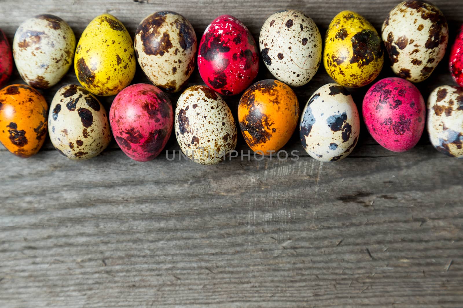 Multi-color dyed easter eggs arranged in a row on wooden background. Easter background with space for a text.