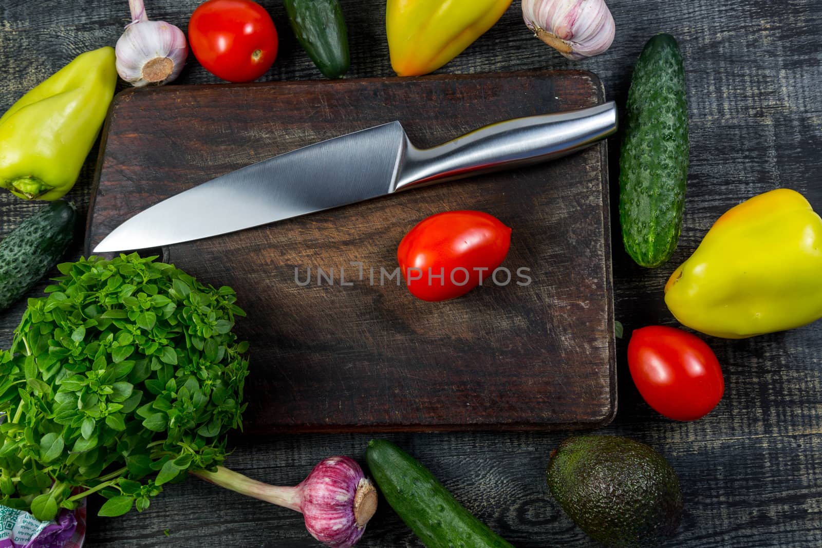 High Angle Still Life View of Knife and Wooden Cutting Board Surrounded by Fresh Herbs and Assortment of Raw Vegetables on Rustic Wood Table