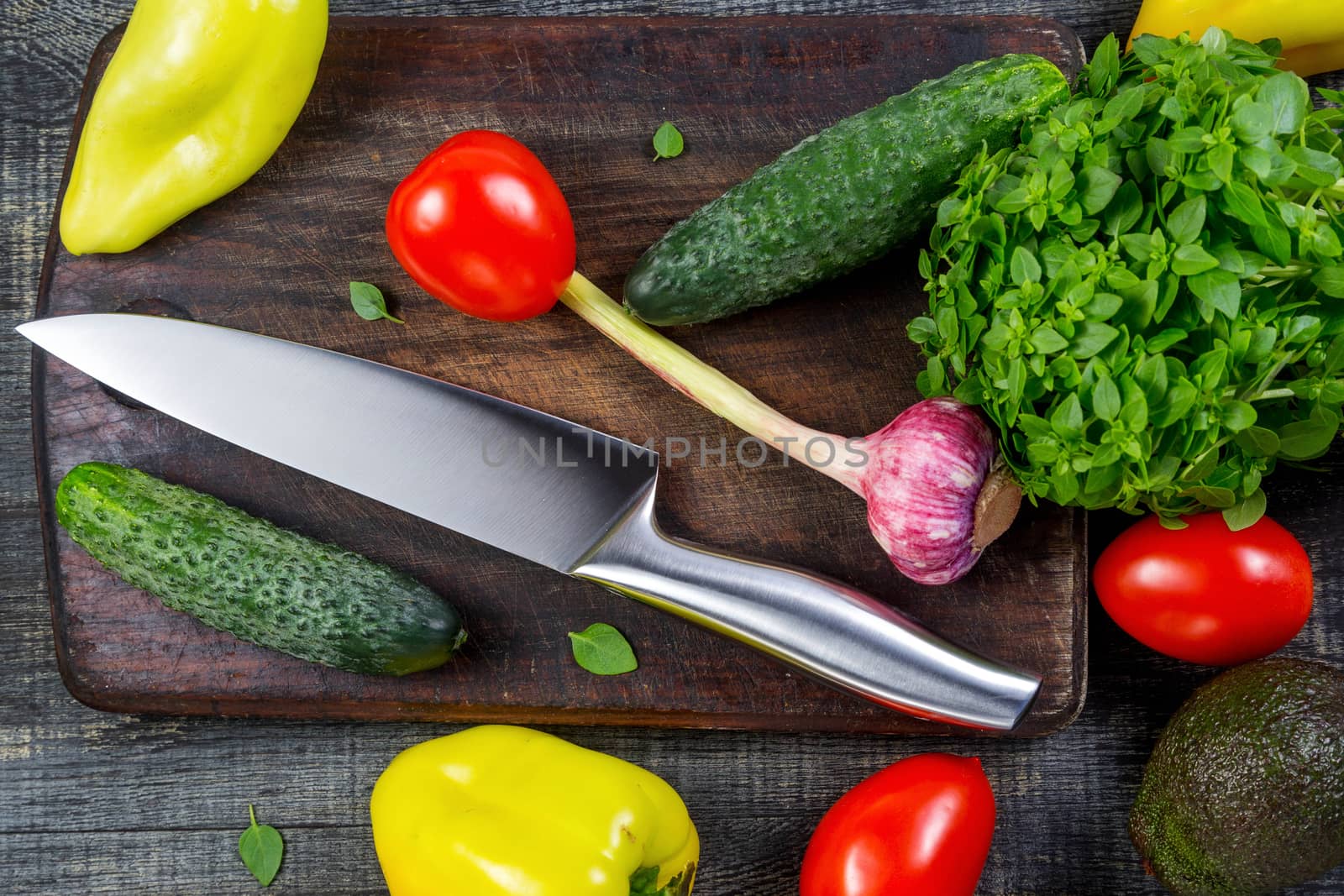 High Angle Still Life View of Knife and Wooden Cutting Board Surrounded by Fresh Herbs and Assortment of Raw Vegetables on Rustic Wood Table