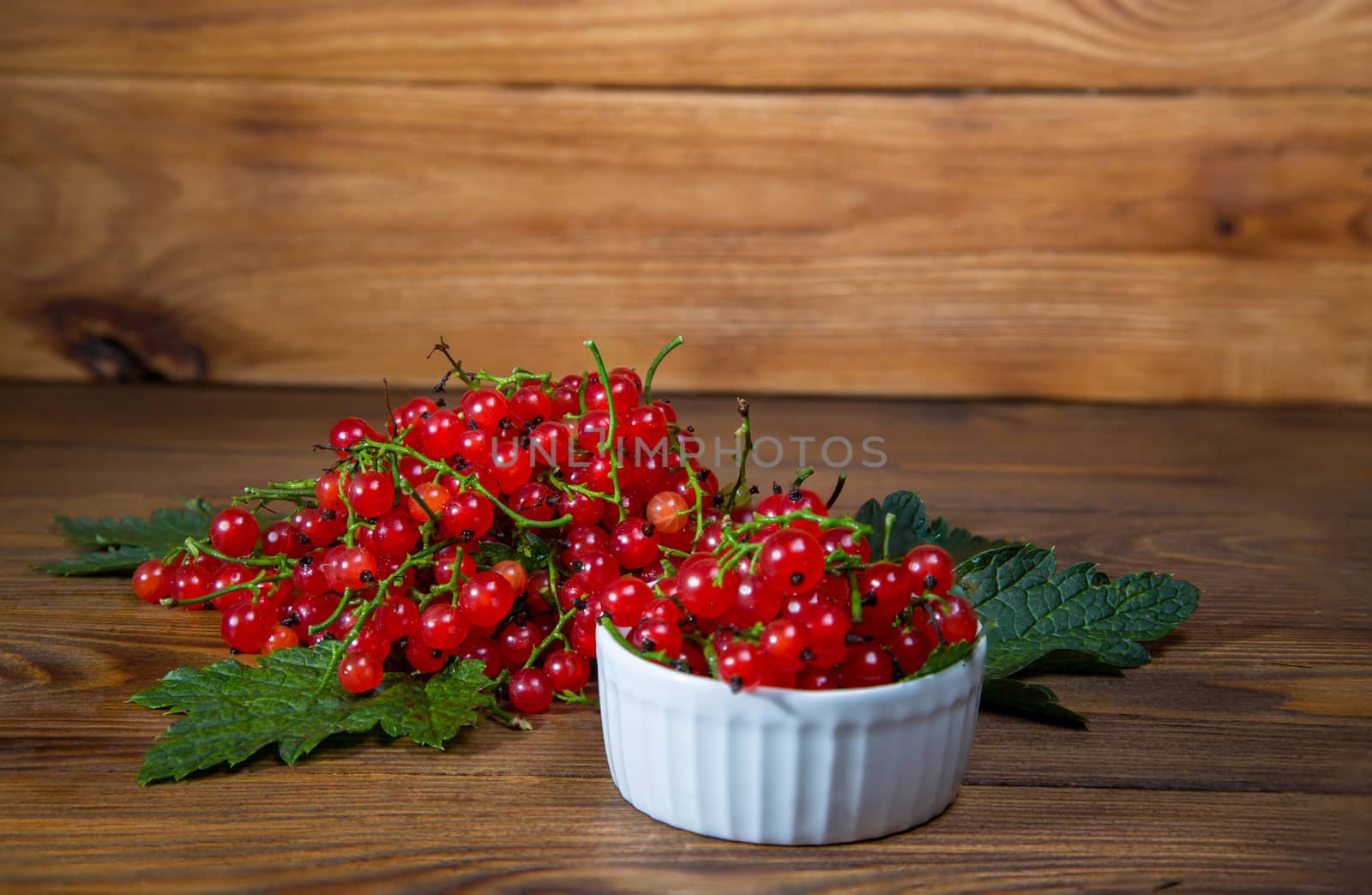 red currant berries in a ceramic bowl on a rustic wooden background. by galinasharapova