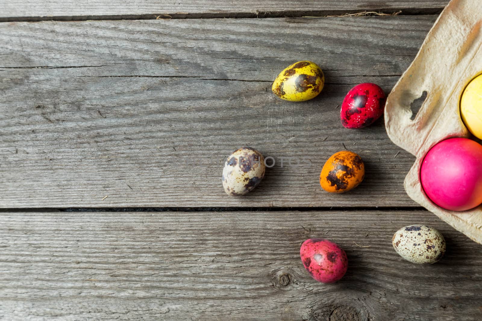 Dyed easter eggs in cardboard box on wooden background. Easter background with space for a text.