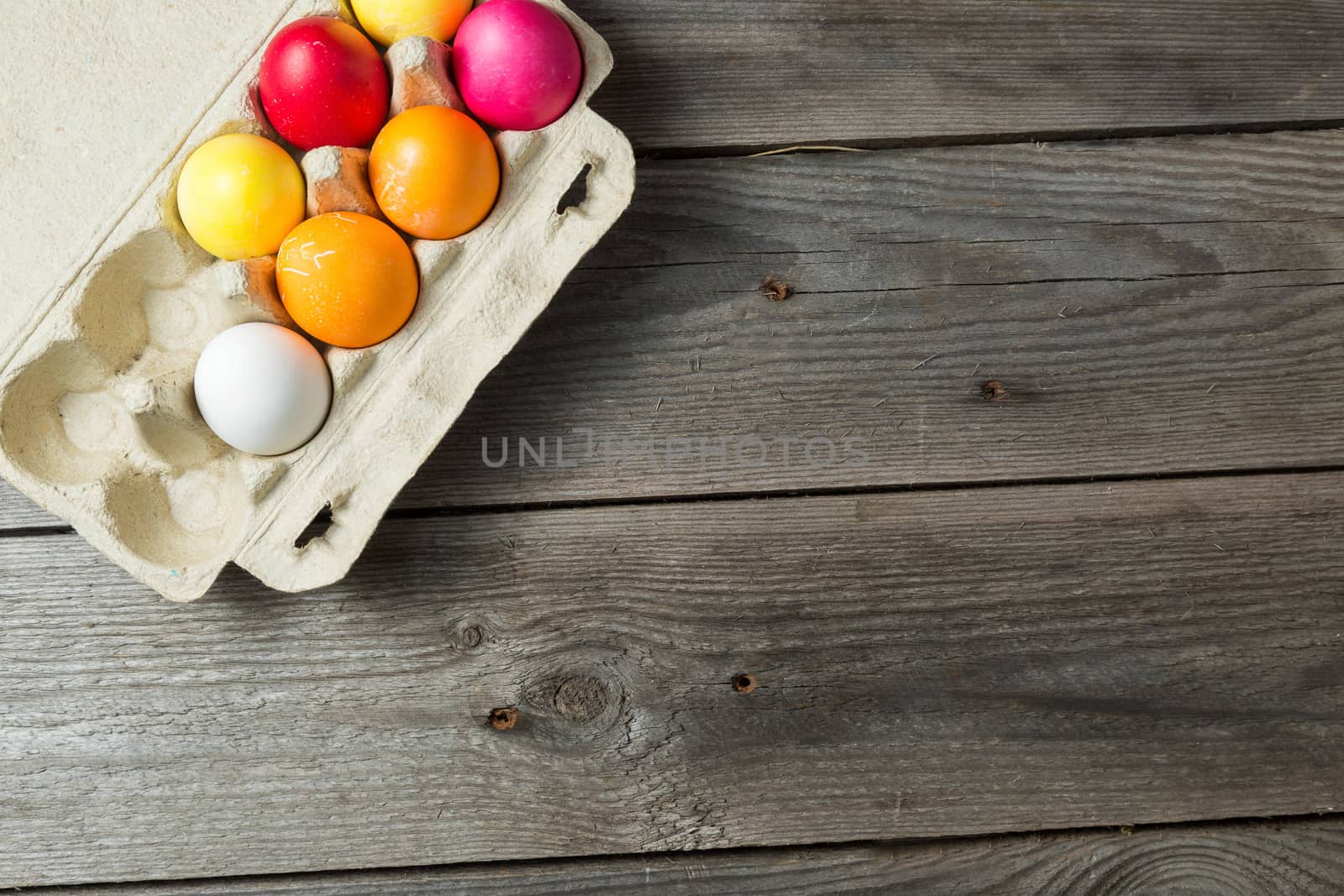 Dyed easter eggs in cardboard box on wooden background. Easter background with space for a text.