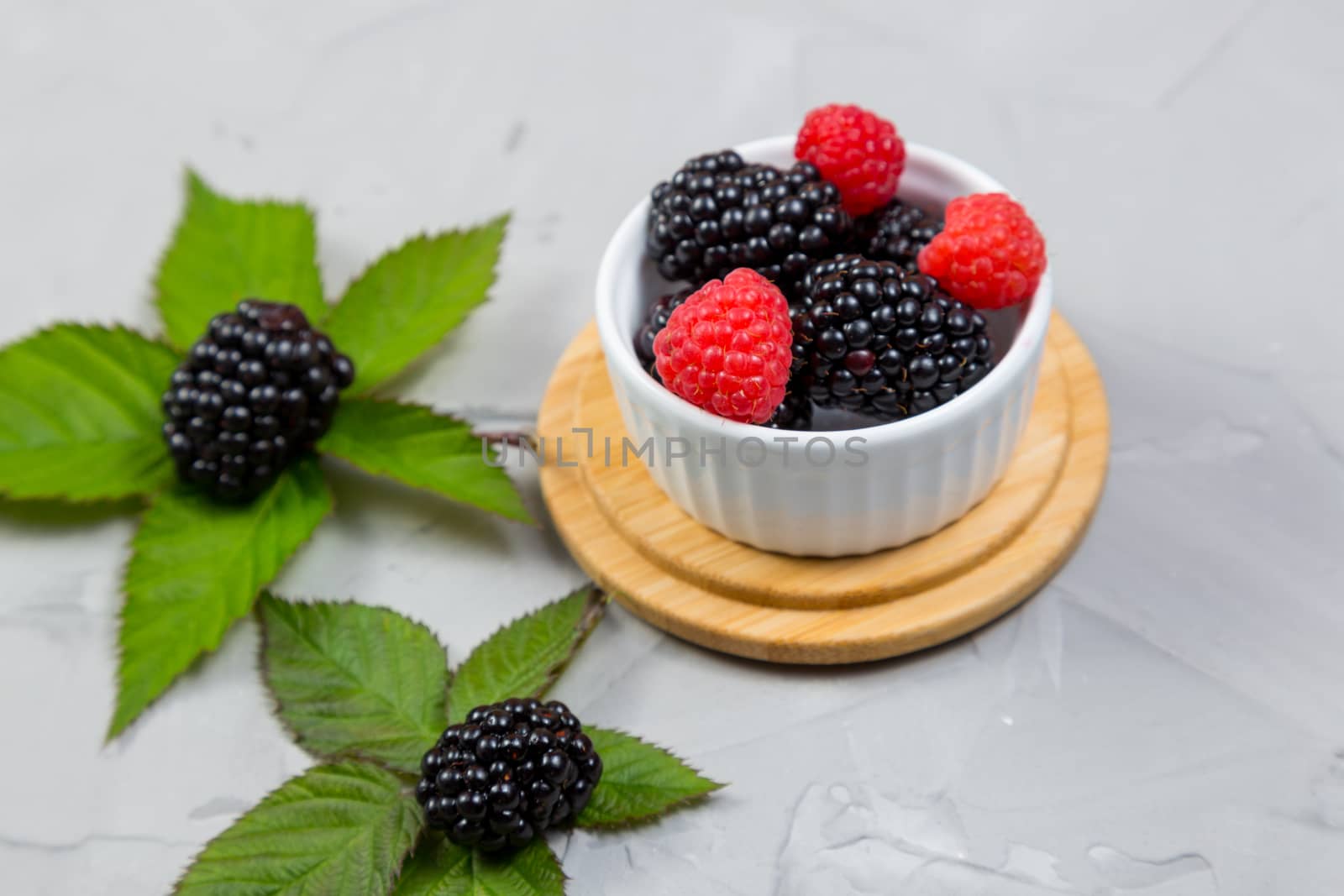 ripe blackberry with leaves on a wooden cutting board in a white ceramic plate on concrete background