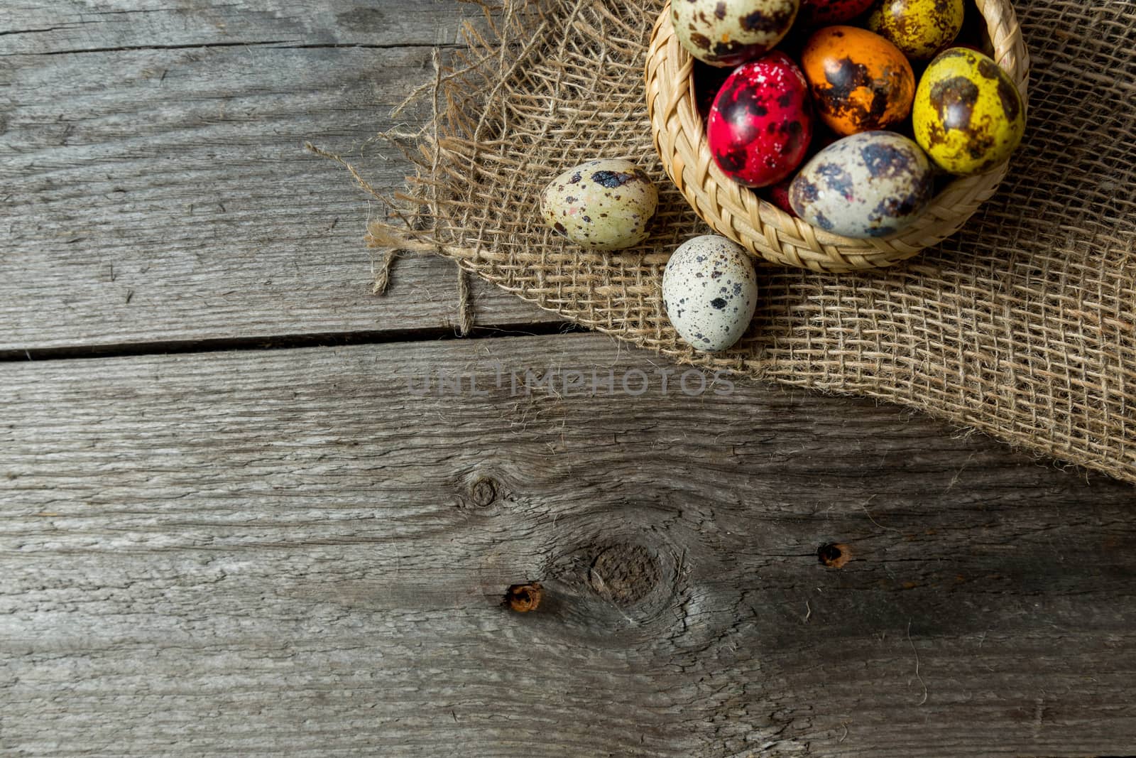 Multi-color dyed Hand painted easter eggs in wicker basket on burlap napkin on wooden background. Easter background with space for a text.