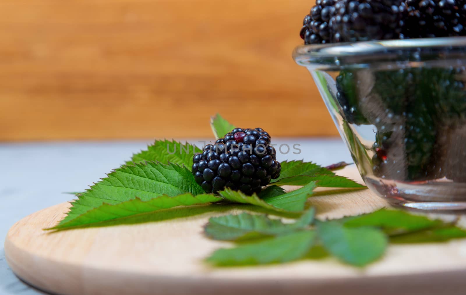 ripe blackberries with leaves in a glass bowl on a bamboo cutting board on a concrete background, rustic, selective focus
