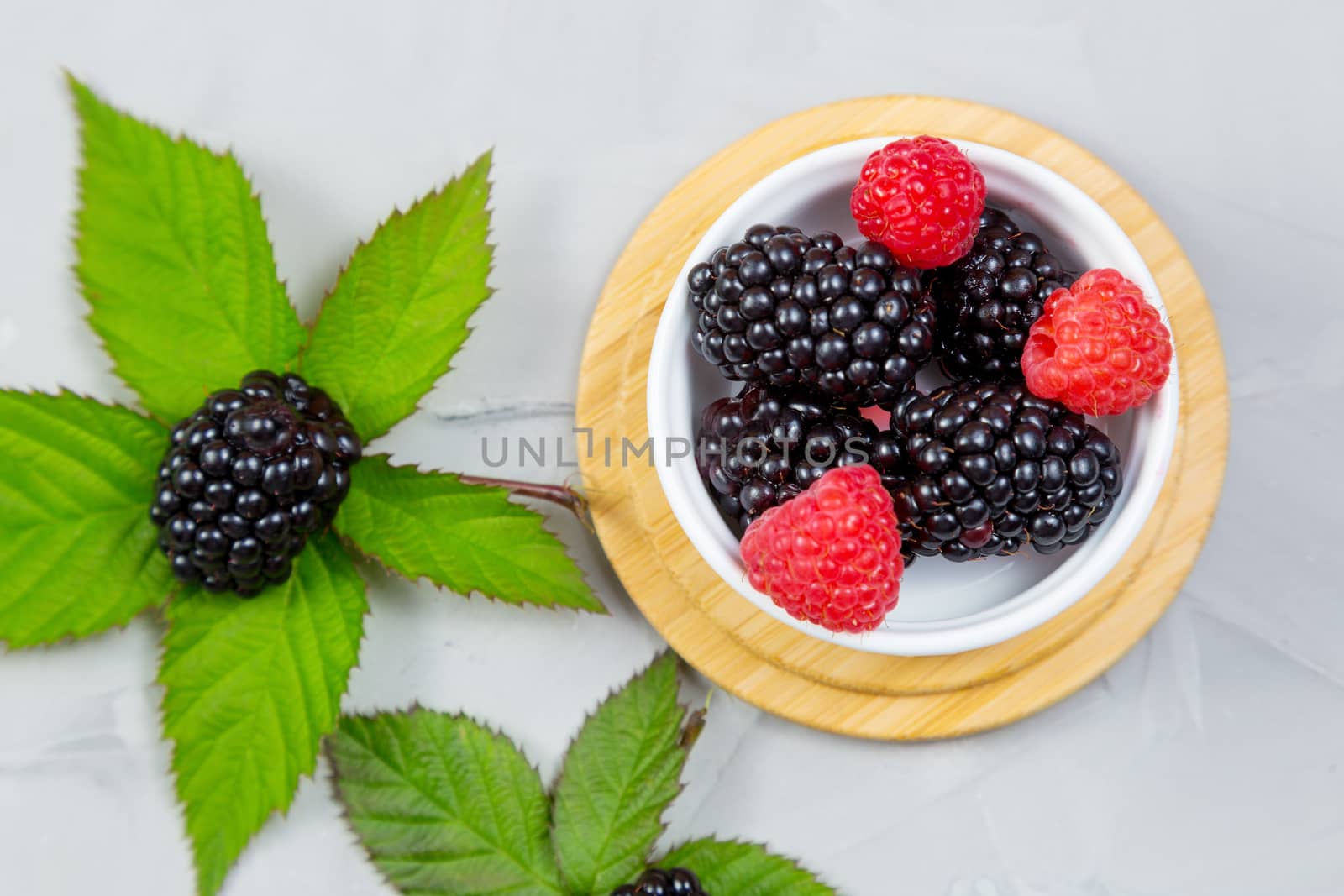 ripe blackberry with leaves on a wooden cutting board in a white ceramic plate on concrete background