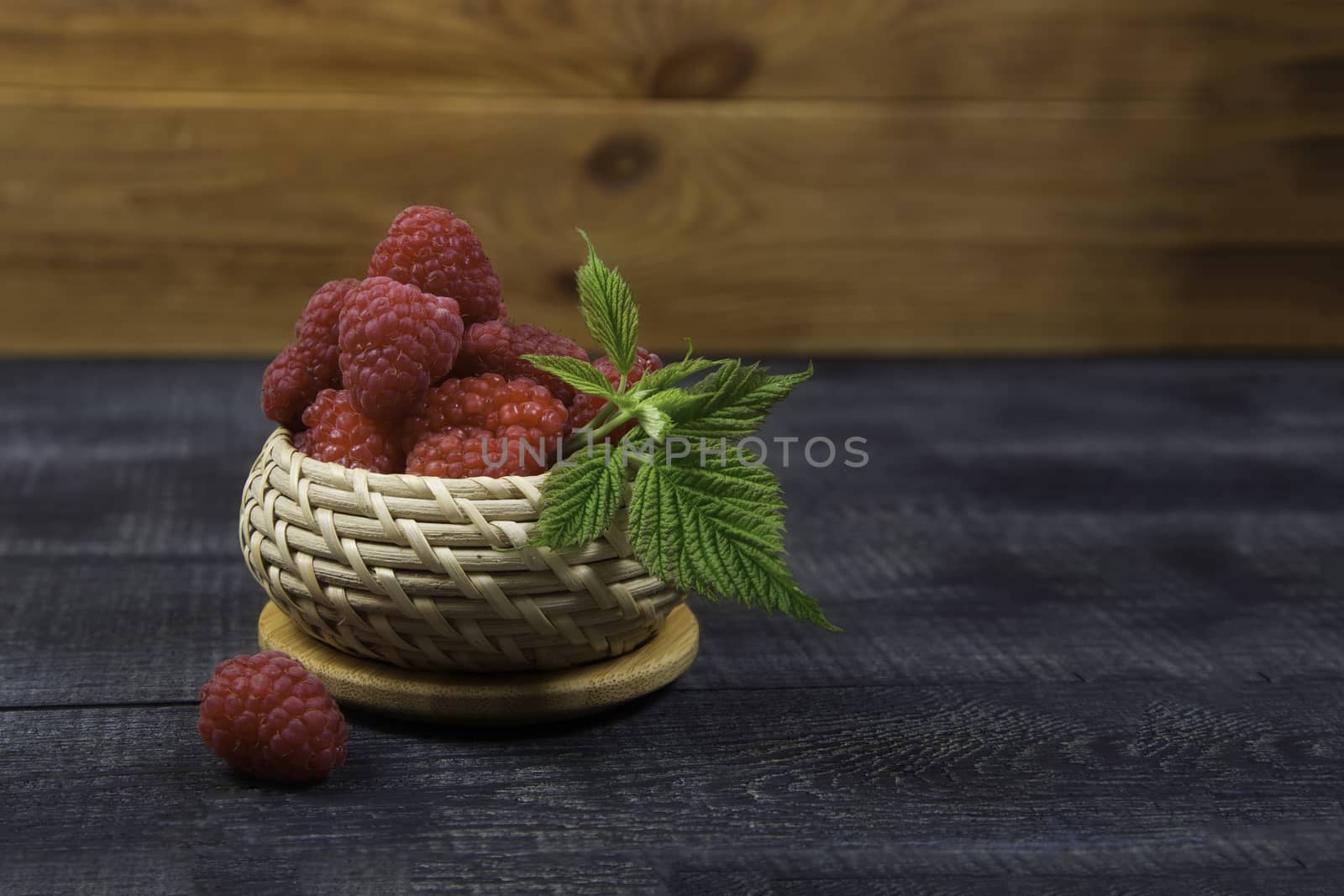 Ripe tasty bright Fresh raspberry in a wicker basket on a cutting board on a wooden background