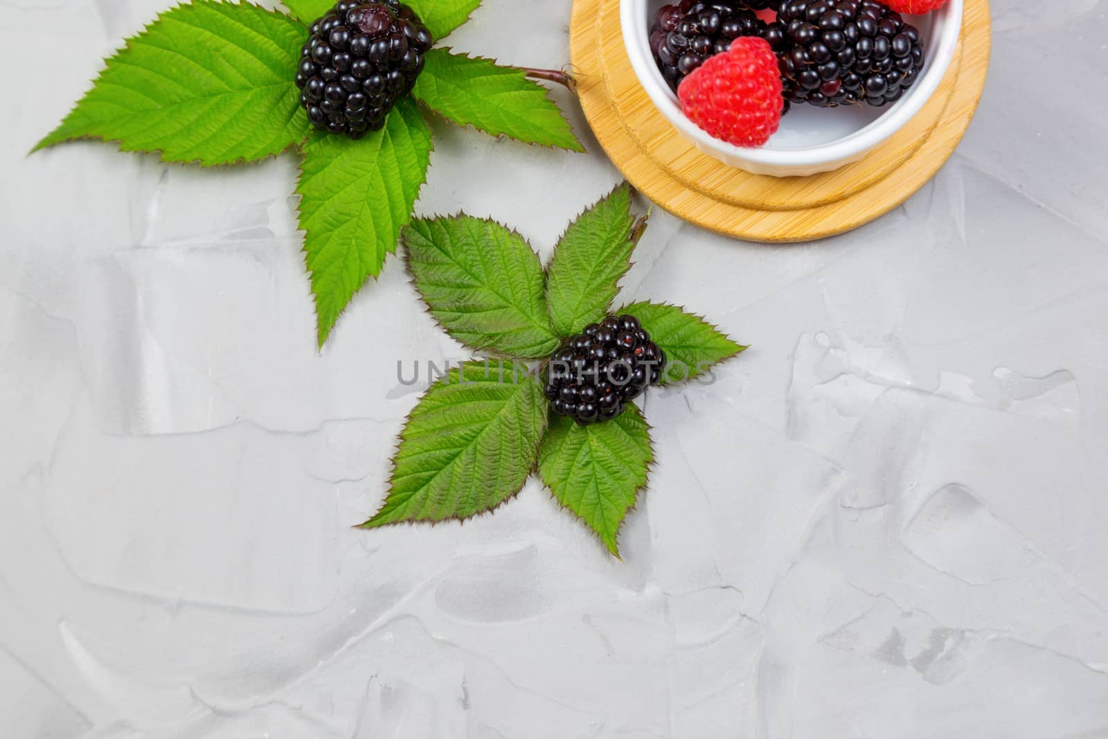 ripe blackberry with leaves on a wooden cutting board in a white ceramic plate on concrete background place for text, selective focus