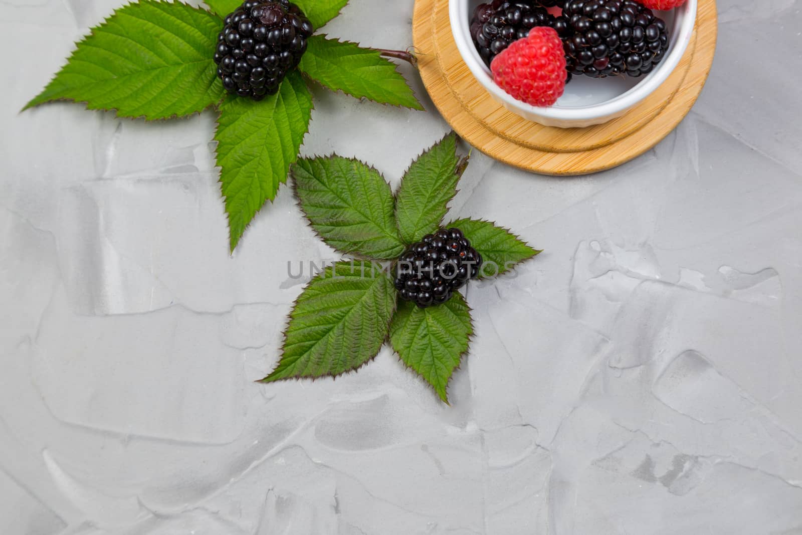 .ripe blackberry with leaves on a wooden cutting board in a white ceramic plate on concrete background place for text