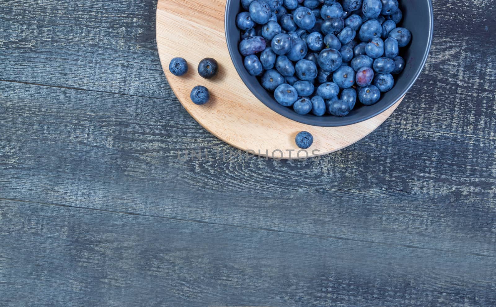 blueberry berry in dark gray ceramic bowl on wooden cutting board on dark blue wooden background. top view, place for text