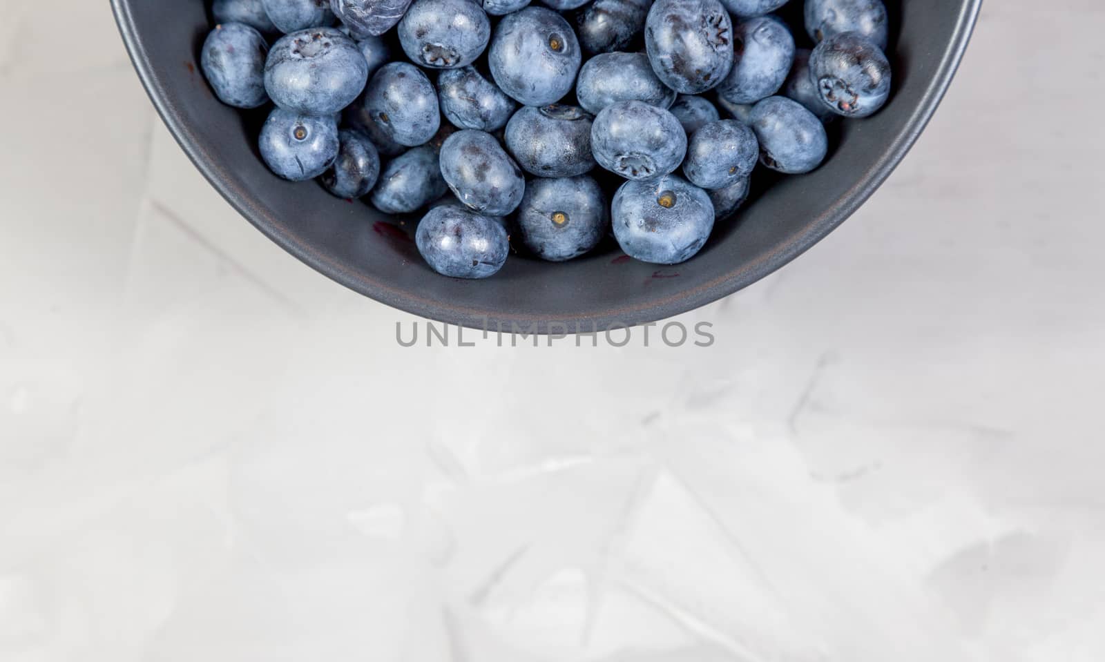 blueberry berry in dark gray ceramic bowl on gray concrete background, place for text