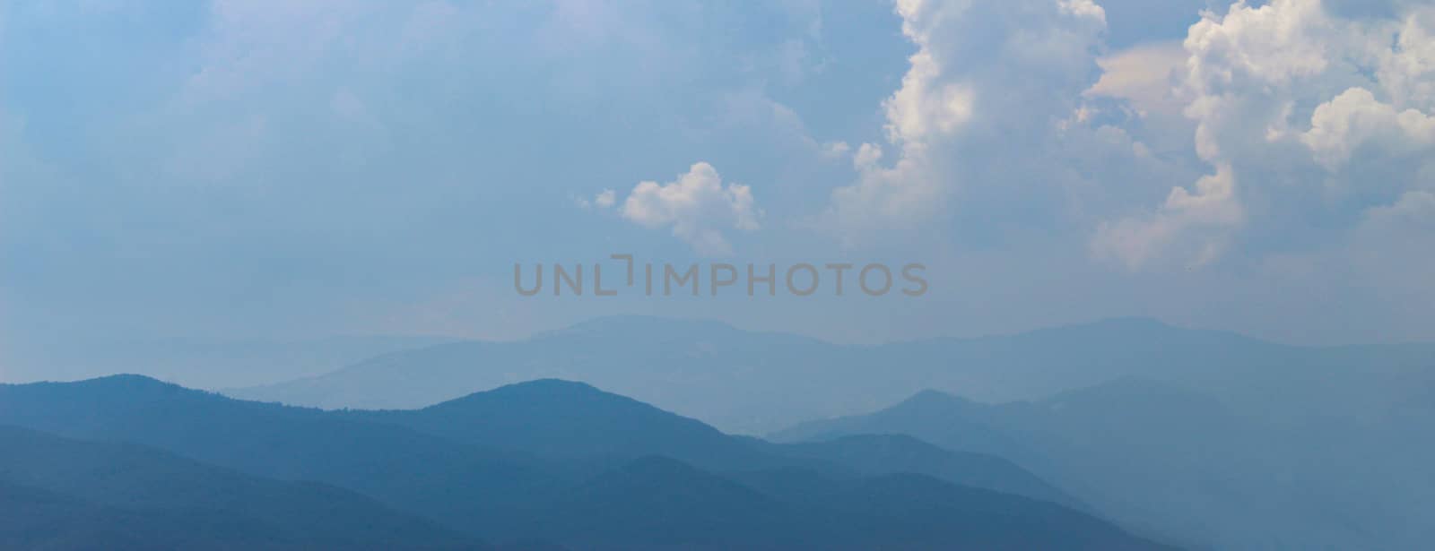 Banner. Blue silhouette of a mountain in the distance, with clouds in the blue sky. Mountains and hills in the distance. by mahirrov
