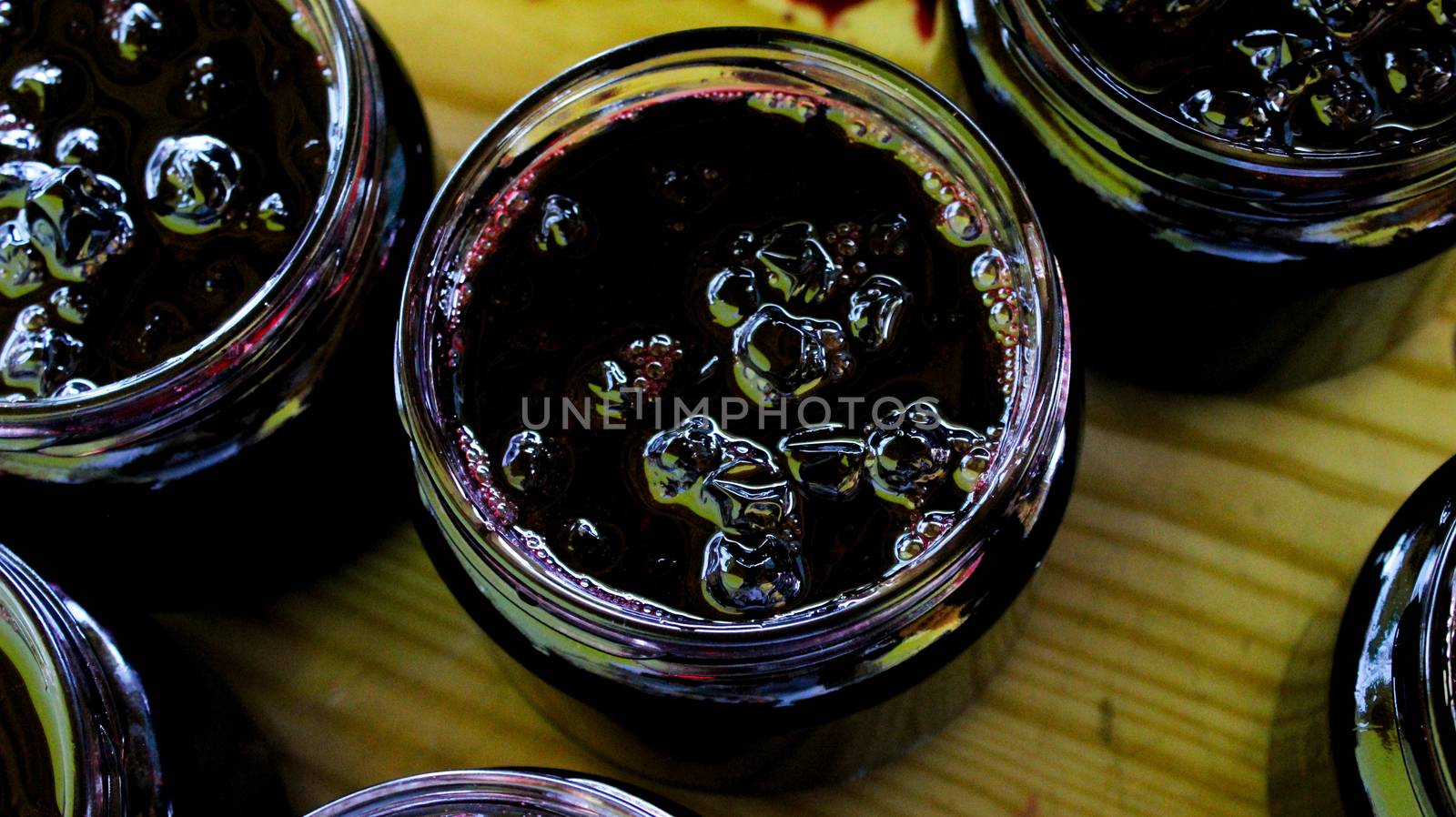The process of filling homemade chokeberry jam on a tray. Banner. Jars full of aronia jam, ready to close. Zavidovici, Bosnia and Herzegovina.